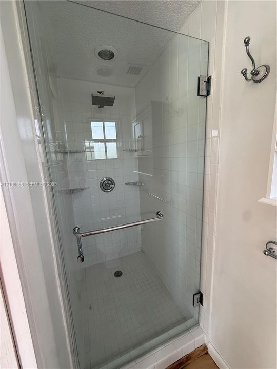 Walk-in shower featuring a frameless glass door, rain-style showerhead, tiled walls, built-in corner shelving, and a chrome towel bar