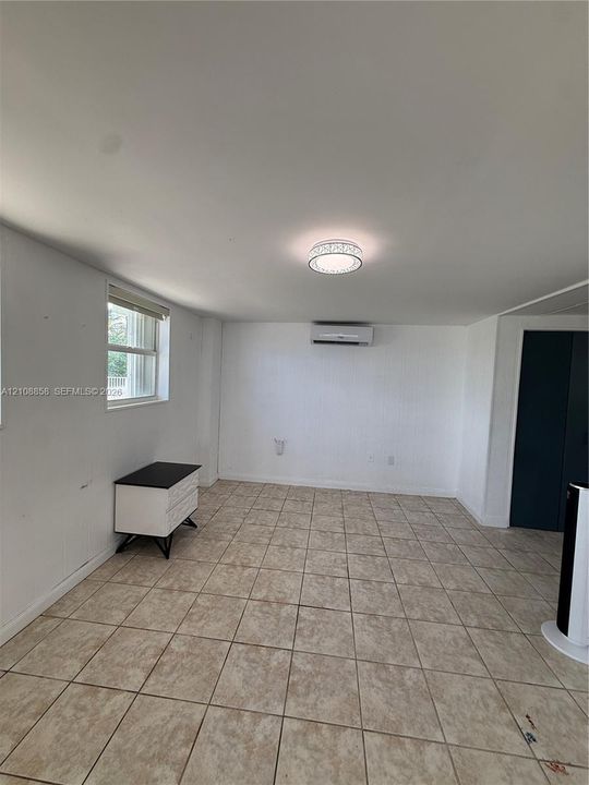 Interior space featuring neutral tile flooring, a wall-mounted mini-split HVAC system, a flush-mount circular light fixture, and a window with a horizontal blind