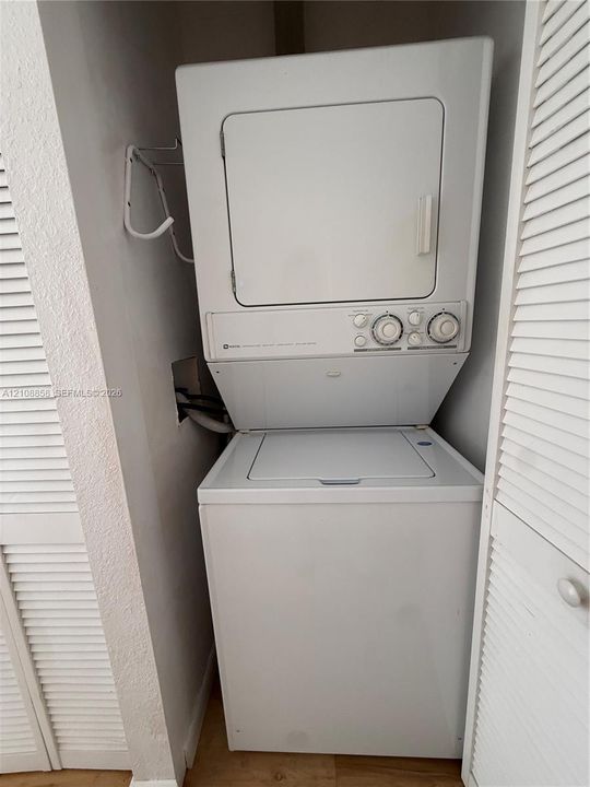 Stacked white washer and dryer unit enclosed by bi-fold louvered doors