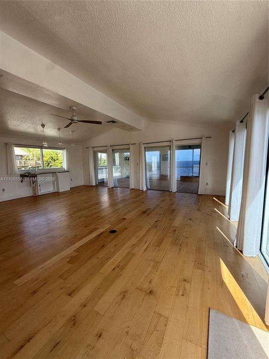 Spacious interior featuring wood-finish flooring, vaulted ceilings, multiple sliding glass doors, a ceiling fan, and built-in cabinetry with a countertop