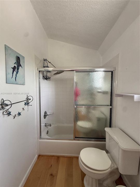 Bathroom featuring a shower-tub combination with white tile surround, glass sliding doors, and wood-finish flooring