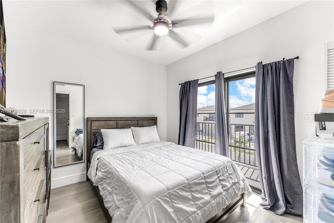 Room featuring wood-finish flooring, a ceiling fan with integrated lighting, and a sliding glass door providing access to a balcony with metal railing