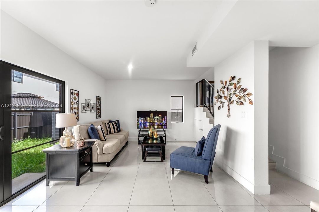 Living area featuring large-format tile flooring, sliding glass door access to the rear exterior, and an open staircase with a metal railing