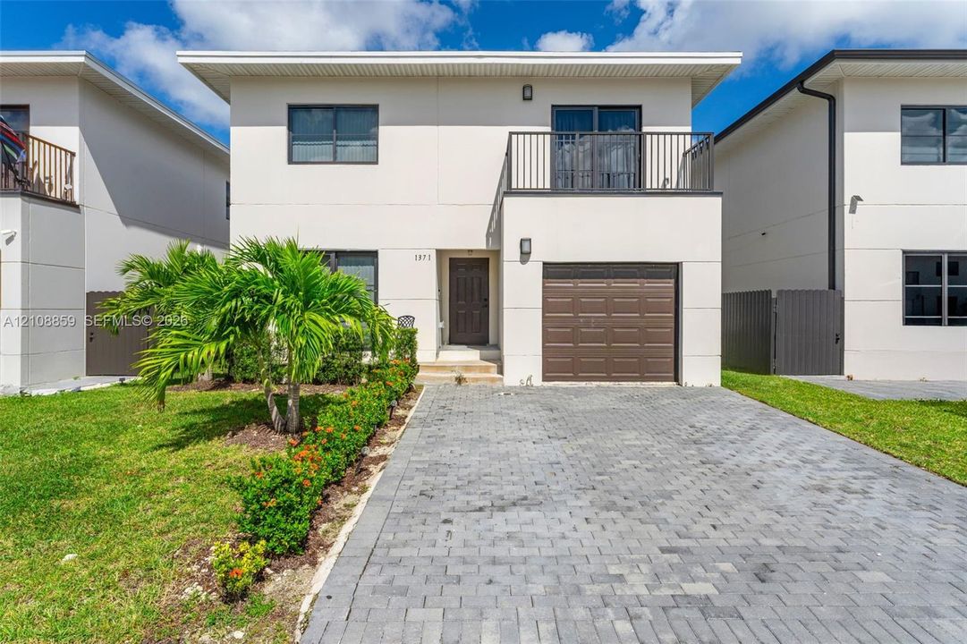 Two-story residence featuring a smooth stucco exterior, a paved stone driveway, an attached garage, and a second-story metal-railed balcony