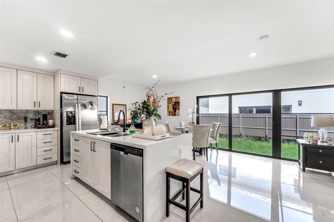 Kitchen featuring light-finish cabinetry, stone-surface countertops, stainless steel appliances, large-format tile flooring, and sliding glass doors