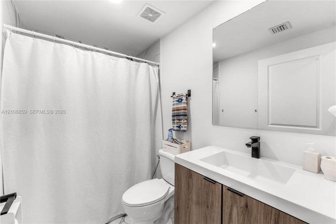 Modern vanity featuring a wood-finish cabinet, integrated rectangular sink, matte black faucet, and solid white countertop paired with a large frameless mirror