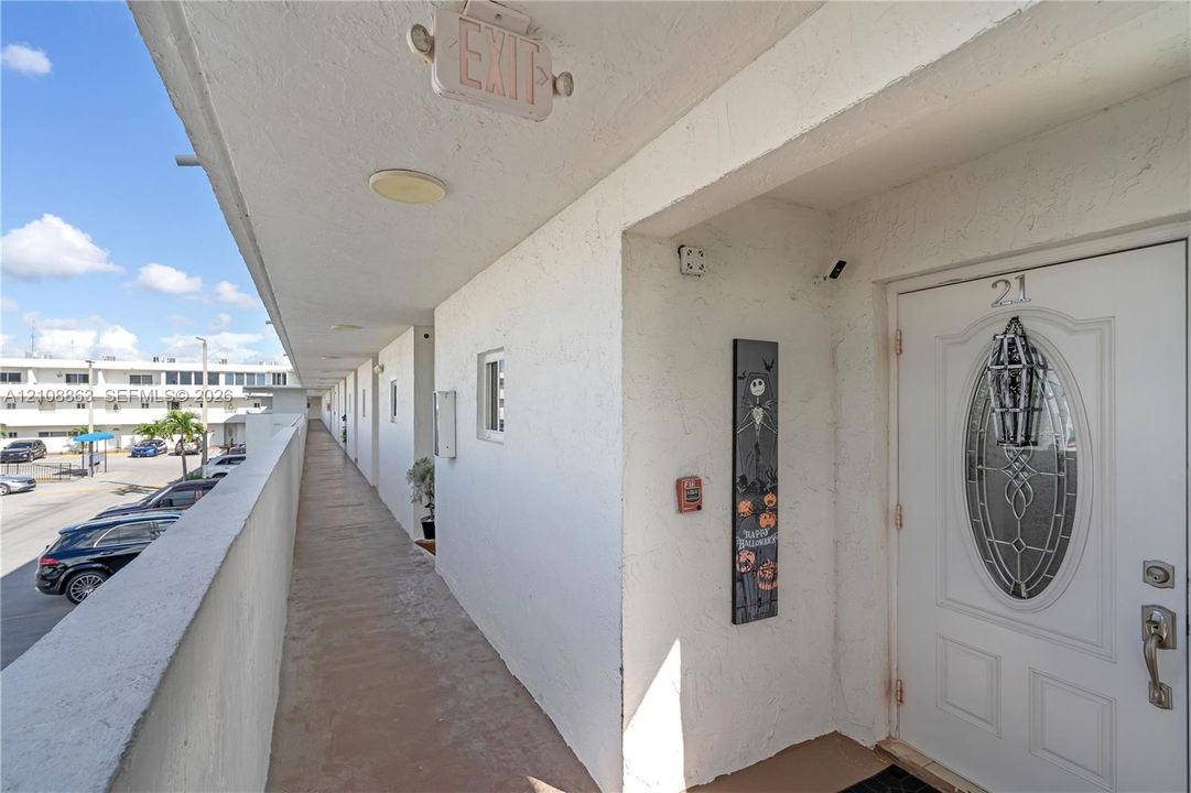 Exterior walkway featuring a stucco facade, white entry door with a decorative oval glass inset, and a metal security deadbolt