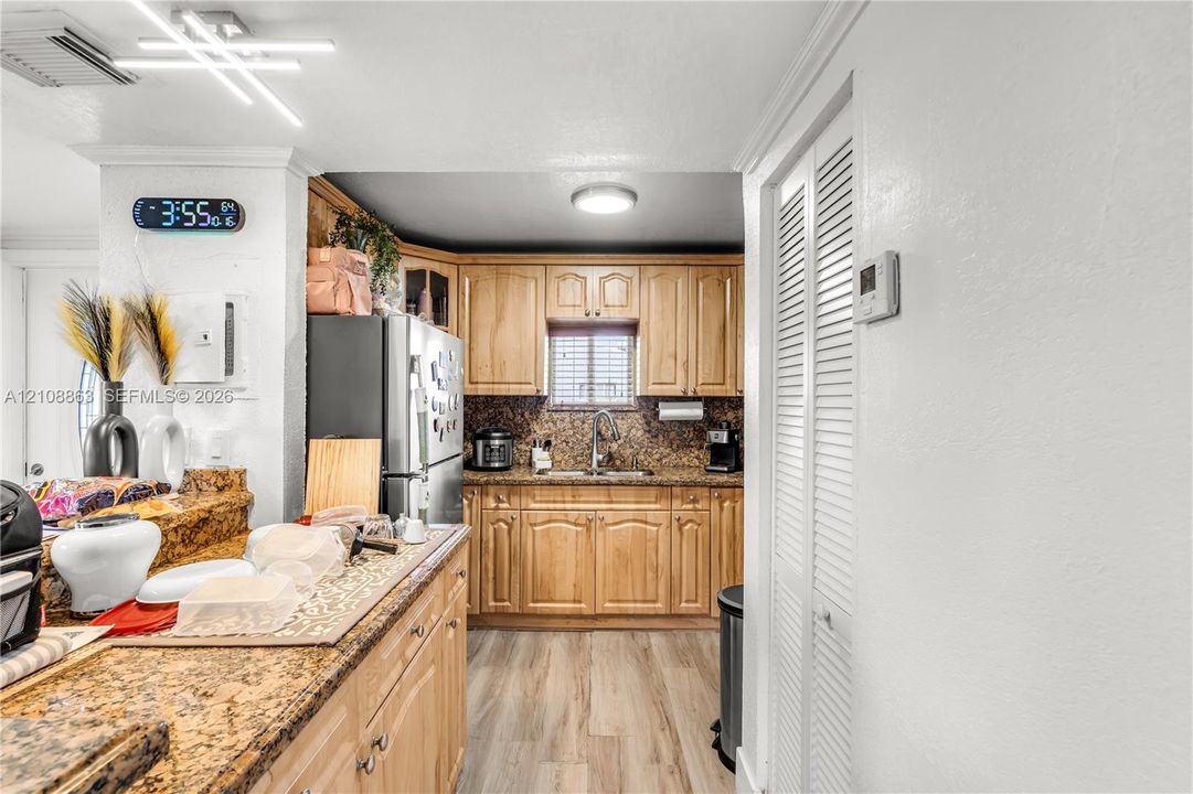 Kitchen featuring light wood cabinetry, stone countertops, integrated stainless steel appliances, wood-finish flooring, and louvered bi-fold doors