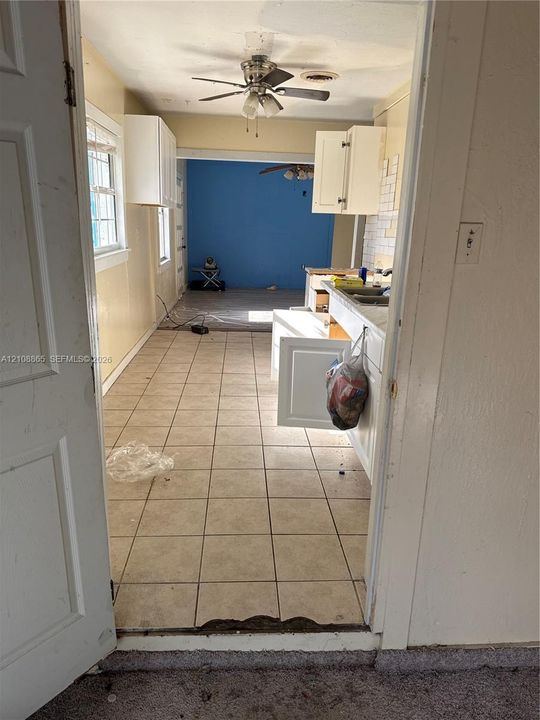 Kitchen featuring light-toned tile flooring, white shaker-style cabinetry, a double-basin stainless steel sink, and a ceiling-mounted light fixture with a fan