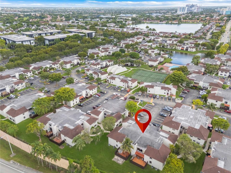 Aerial perspective of multi-unit residential property featuring low-rise architectural design, proximity to community tennis courts, and landscaped green space