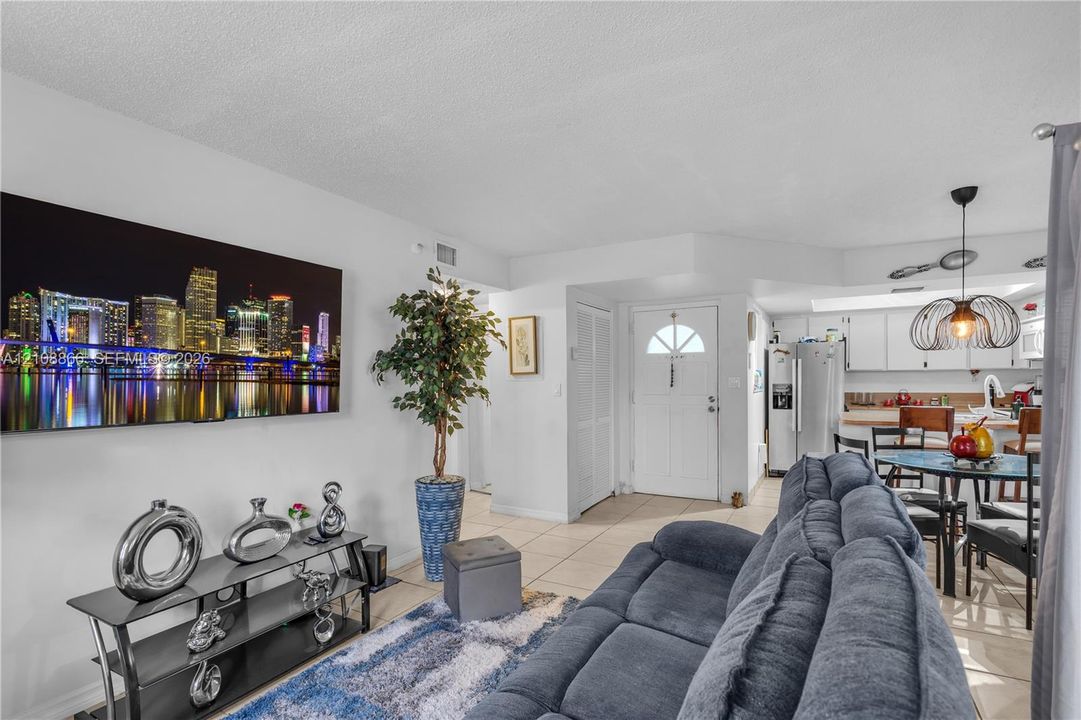 Open-concept area featuring neutral tile flooring, white cabinetry, a kitchen island, and a distinctive pendant light fixture