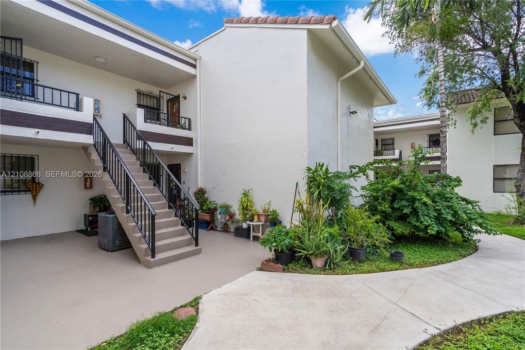 Stucco exterior with multi-level balconies, metal railings, exterior staircase, concrete walkways, and mature landscaping