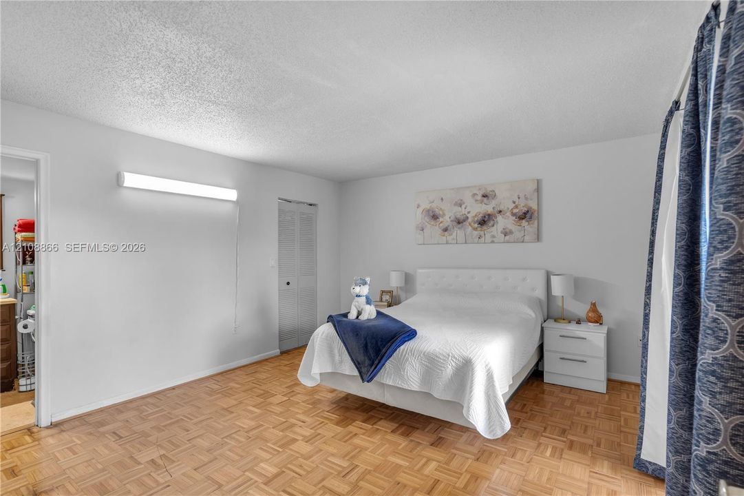 Parquet wood-finish flooring, textured ceiling, wall-mounted linear light fixture, and louvered-panel closet doors