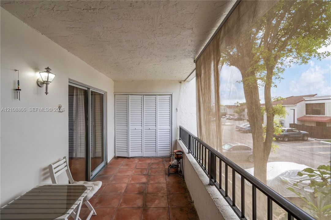 Covered balcony featuring terracotta-style tile flooring, white bi-fold doors, a black metal railing, and an exterior wall-mounted lantern light