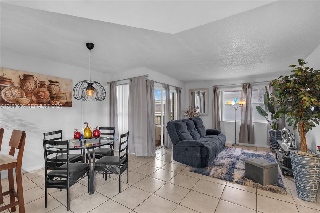 Open-concept space featuring neutral ceramic tile flooring, tray ceilings, and an industrial-style metal pendant light fixture