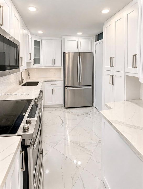Kitchen featuring white shaker-style cabinetry, solid-surface countertops with a subway tile backsplash, stainless steel appliances, and large-format tile flooring