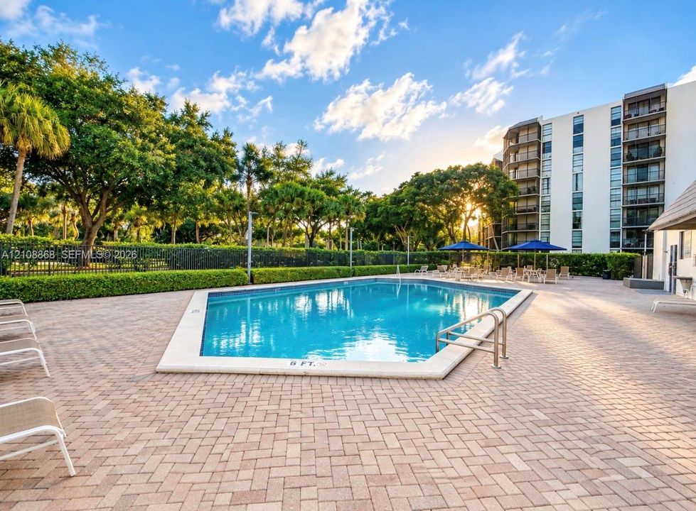 Swimming pool with a stone coping border, surrounding brick-paver patio, and mature landscaping