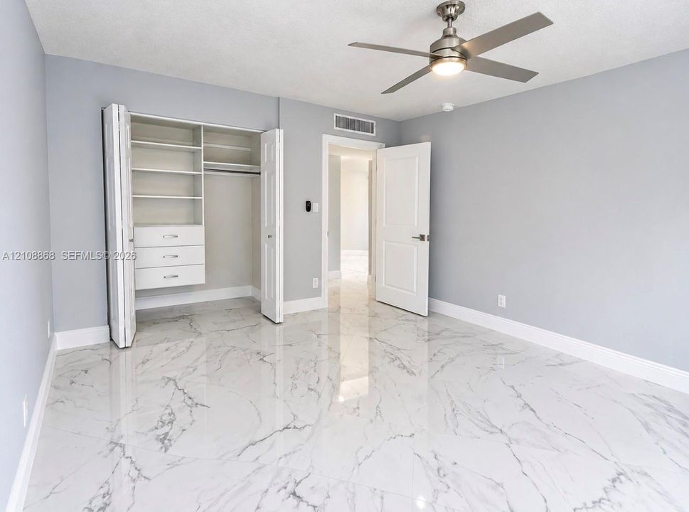 2nd bedroom Large-format tile flooring with a veined finish, built-in closet shelving and drawer system, and brushed nickel ceiling fan with integrated lighting