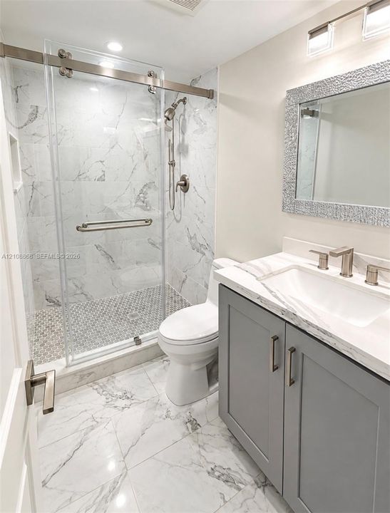2nd bath Bathroom featuring a walk-in shower with sliding glass door, stone-patterned tile flooring, gray shaker-style vanity with stone-composite countertop, and wall-mounted vanity lighting