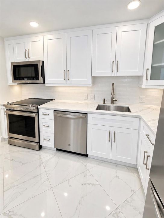 Kitchen featuring white Shaker-style cabinetry, stainless steel appliances, light-toned stone-finish countertops, tiled backsplash, and large-format porcelain tile flooring