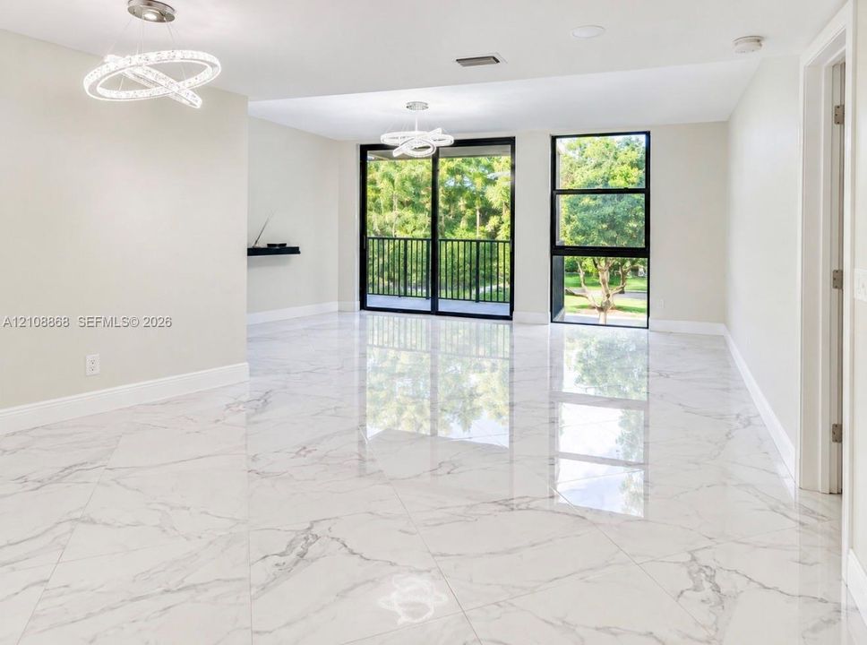 Polished large-format stone-finish flooring, dual contemporary circular LED pendant fixtures, floor-to-ceiling glass sliding balcony door, and black-framed windows