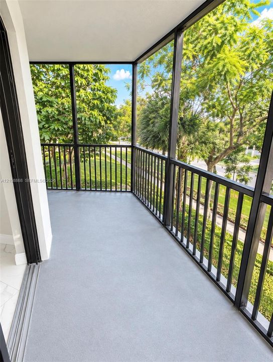 Screened-in wrap around balcony featuring a solid surface floor, black metal railing, and overhead enclosure