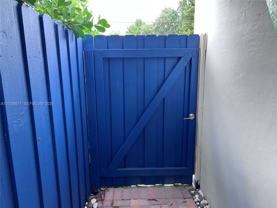 Blue painted wood gate with diagonal bracing, brushed metal handle, and paver stone walkway