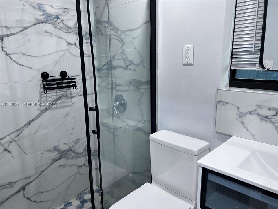 Walk-in shower with black-framed glass enclosure, large-format veined tile surround, and hexagonal floor tile, complemented by a vanity with a white countertop and integrated sink