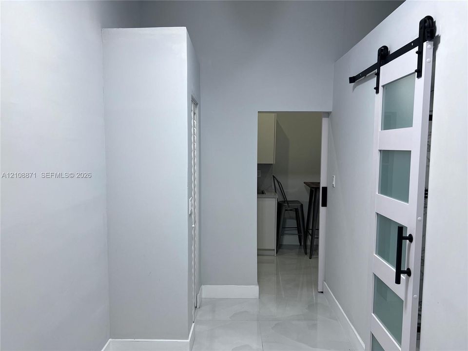 White sliding barn door featuring frosted glass panels and matte black hardware, paired with large-format light-toned flooring