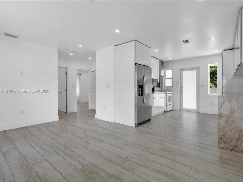 Kitchen featuring high-gloss cabinetry, stainless steel refrigerator, stone-finish kitchen island, recessed lighting, and wood-finish flooring