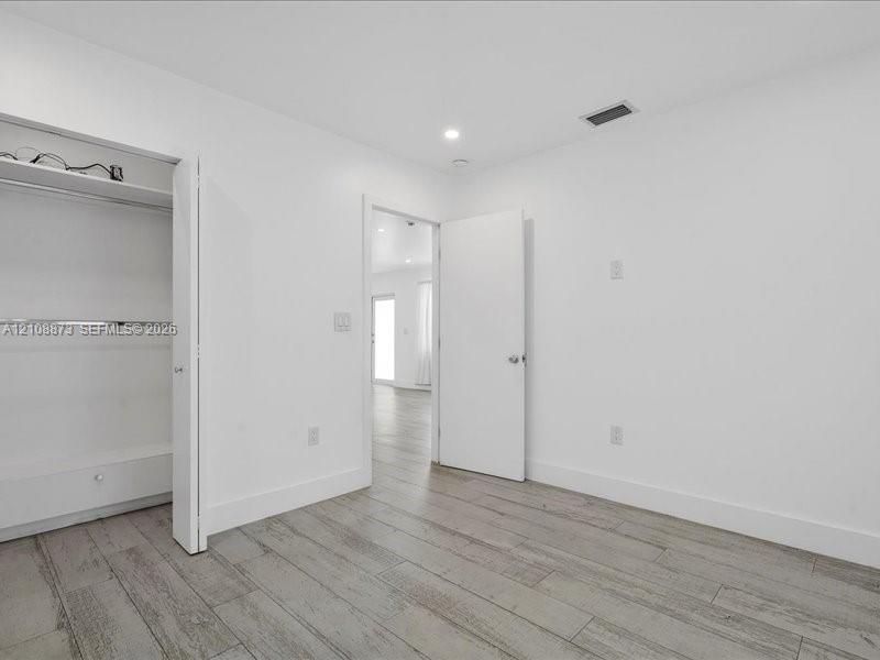 Room interior featuring wood-finish flooring, recessed lighting, and a closet with a built-in shelving unit and metal garment rod