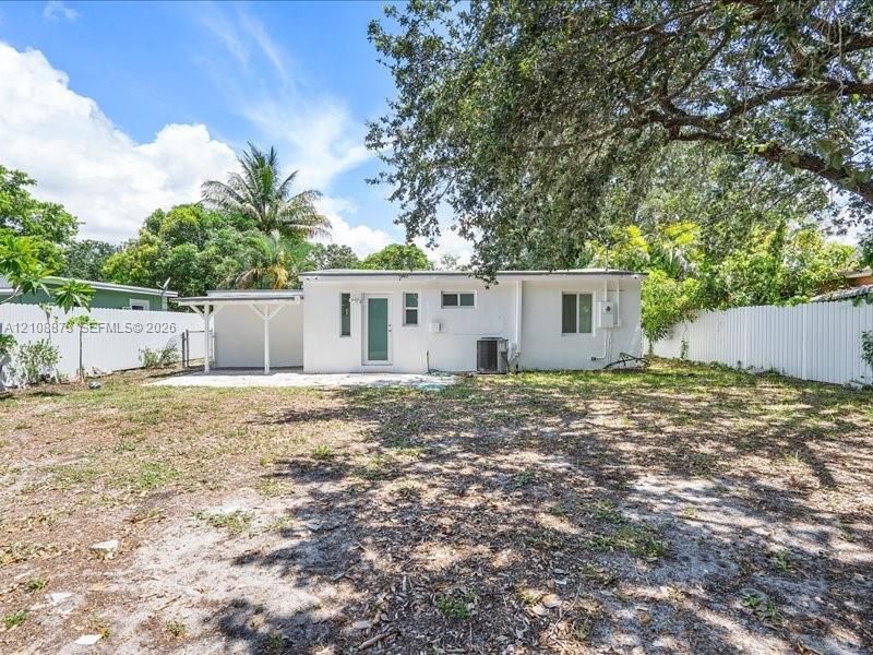 Single-story exterior featuring a white stucco facade, an attached covered carport, and a white vinyl privacy fence enclosing the grounds