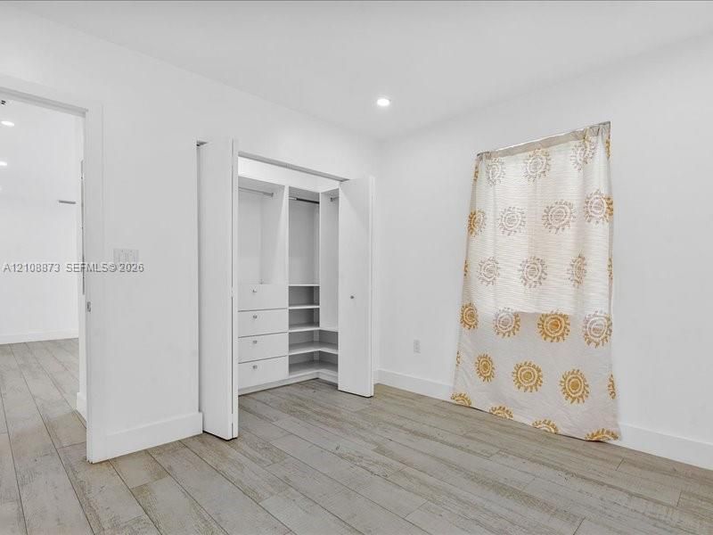 Room interior featuring wood-finish flooring, recessed lighting, and a built-in closet system with integrated shelving and drawer storage
