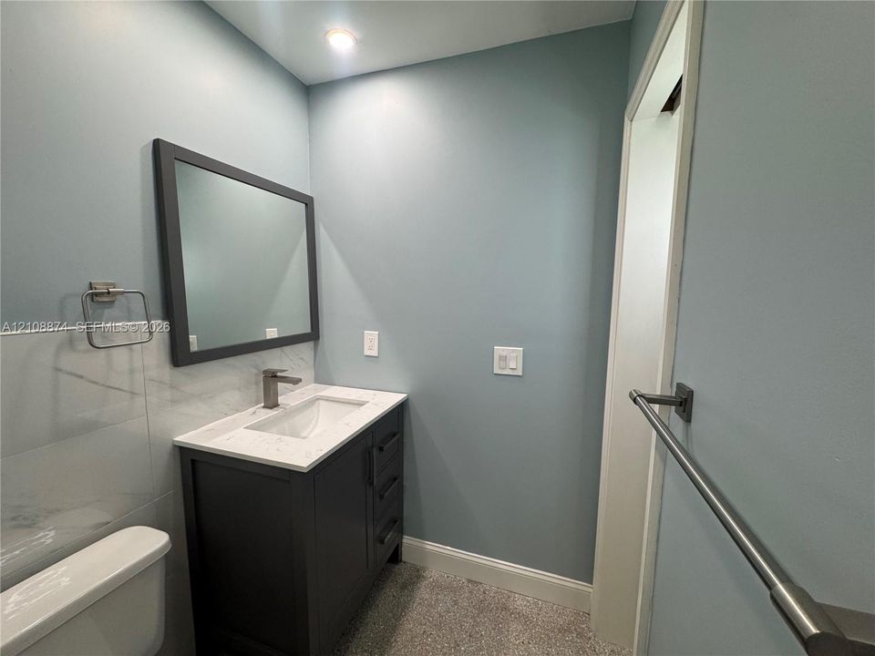 Vanity with a solid surface countertop, undermount sink, dark-finish cabinetry, framed wall mirror, and metal wall-mounted hardware