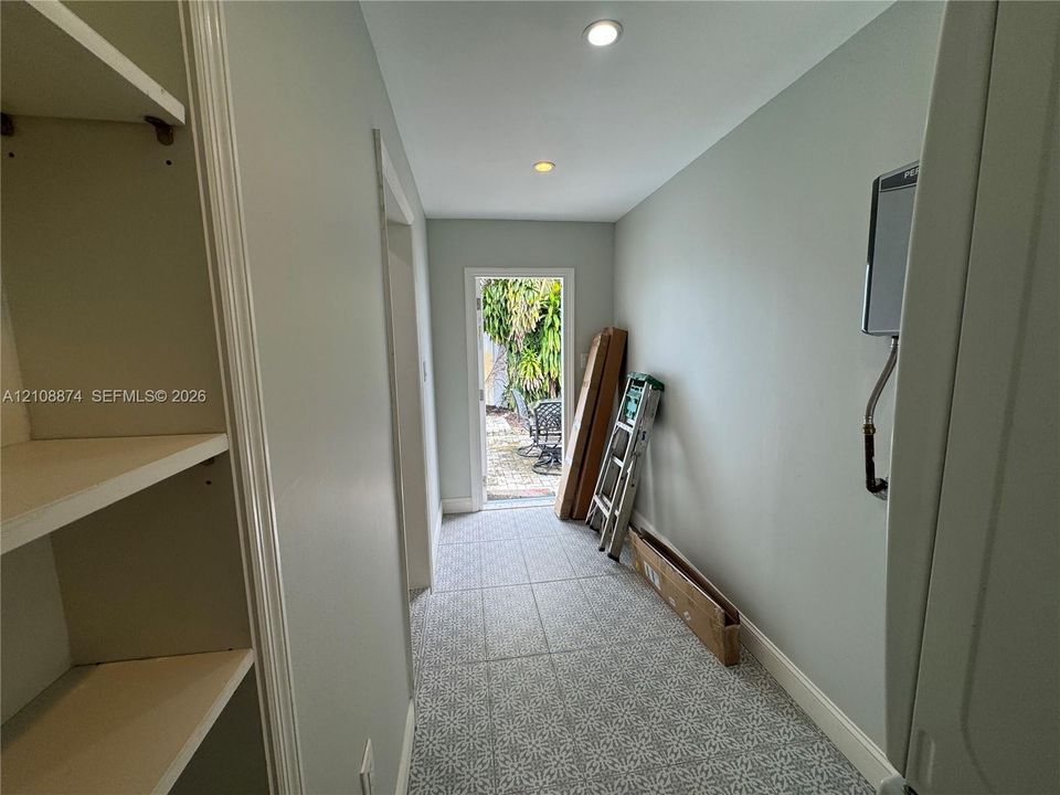 Hallway featuring patterned tile flooring, built-in shelving, recessed ceiling lighting, and a doorway providing egress to the exterior