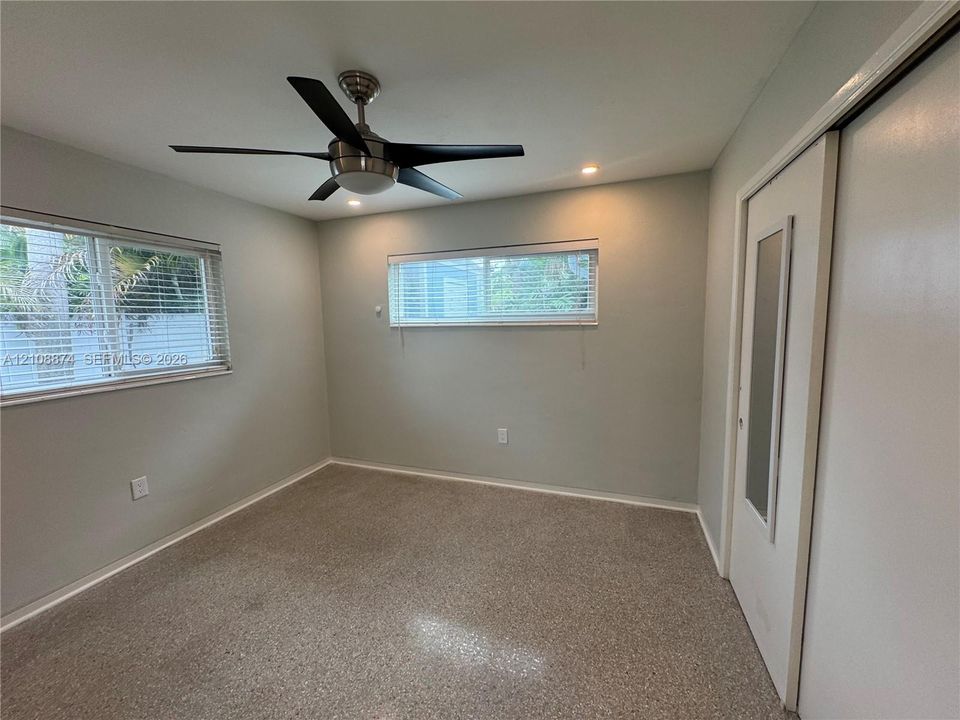 Neutral-toned room featuring a five-blade brushed metal ceiling fan, recessed lighting, horizontal slider windows, and a closet with a glass-paneled door