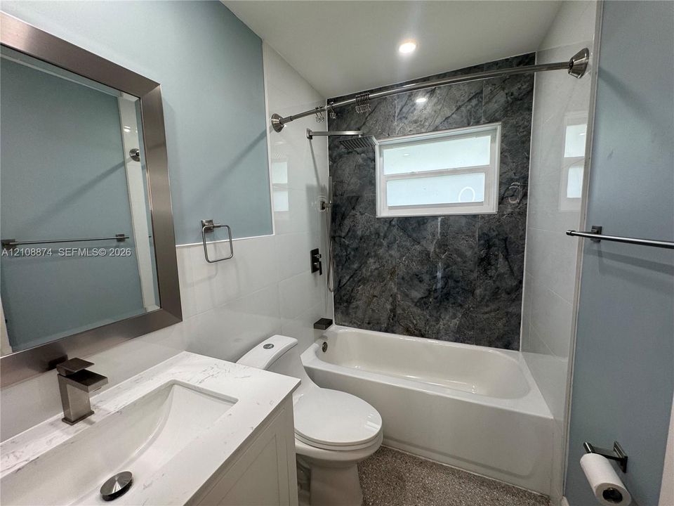Bathroom featuring a white vanity with a stone-top integrated sink, a deep soaking tub with a patterned tile surround, and a framed mirror with metallic finish