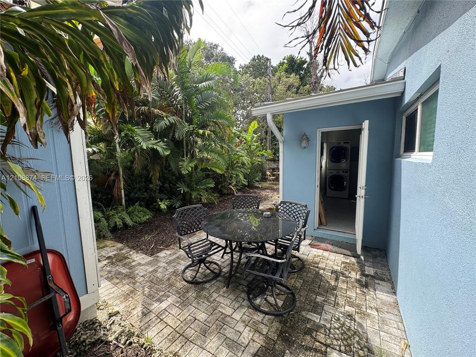 Paved patio featuring a herringbone brick pattern, stucco exterior walls, and a dedicated laundry area with an external entry door