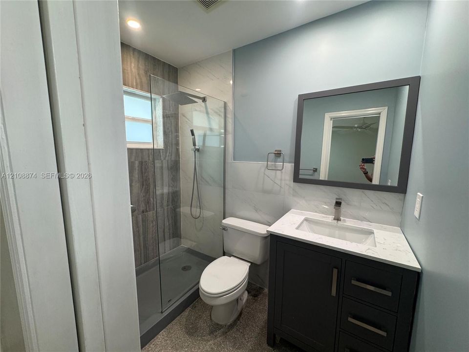 Bathroom featuring a dark vanity with a white countertop and rectangular undermount sink, walk-in shower with floor-to-ceiling tile, glass enclosure, and a wall-mounted rectangular mirror