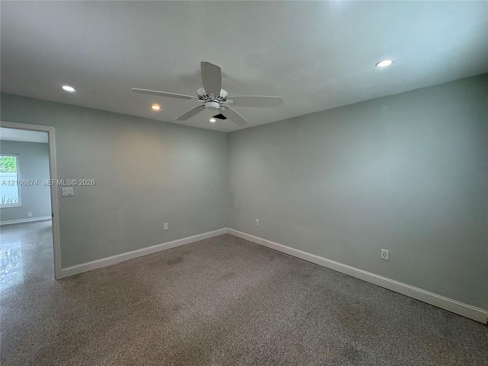 Neutral-toned interior space featuring recessed ceiling lighting, a central white ceiling fan, and carpeted flooring