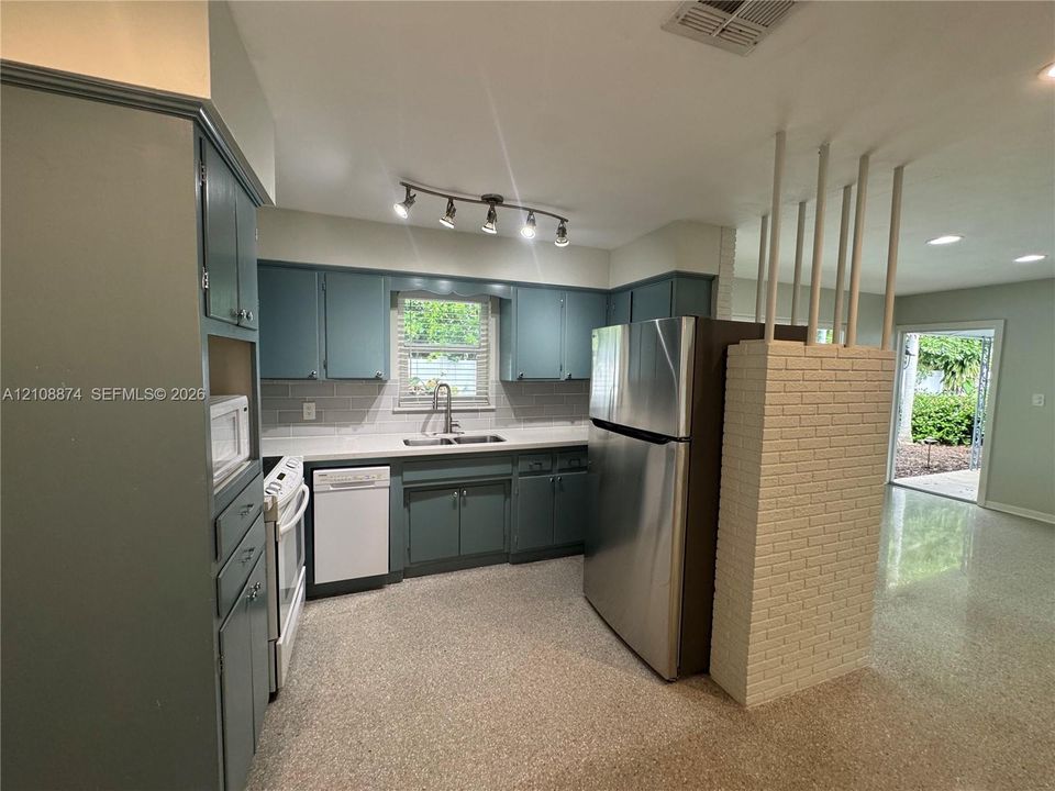 Kitchen featuring blue cabinetry, stone-surface countertops, tile backsplash, stainless steel appliances, and a white brick partition wall