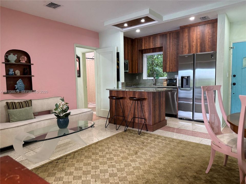Kitchen featuring wood-finish cabinetry, an integrated breakfast bar, stainless steel appliances, and a recessed ceiling feature with integrated lighting, paired with a built-in arched wall niche