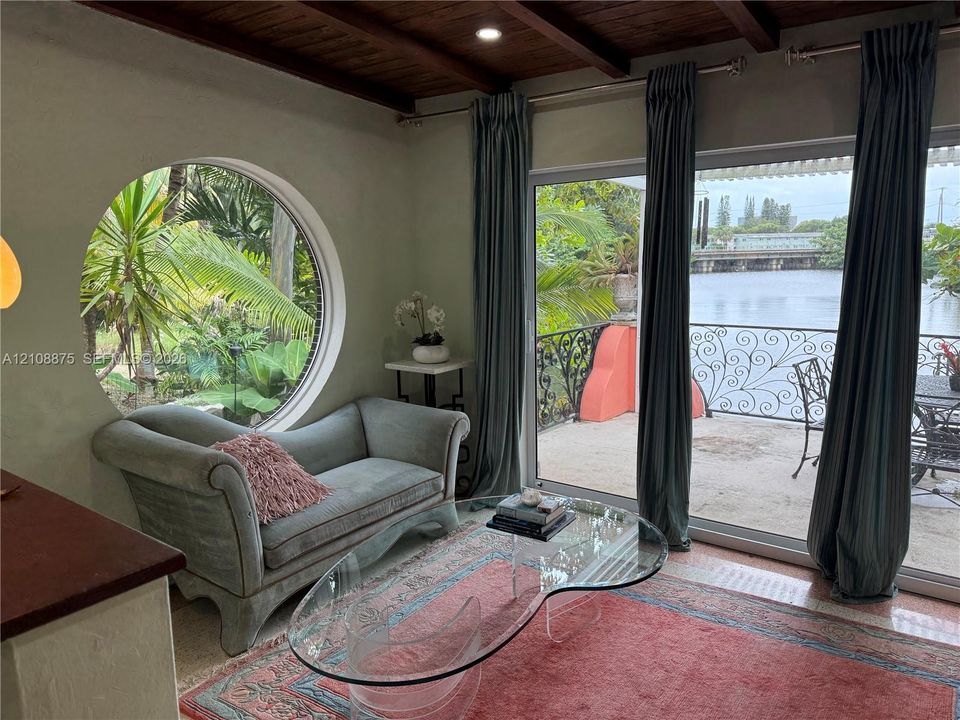 Interior featuring a circular window, exposed wood-beam ceiling, and sliding glass doors opening to a balcony with decorative iron railing
