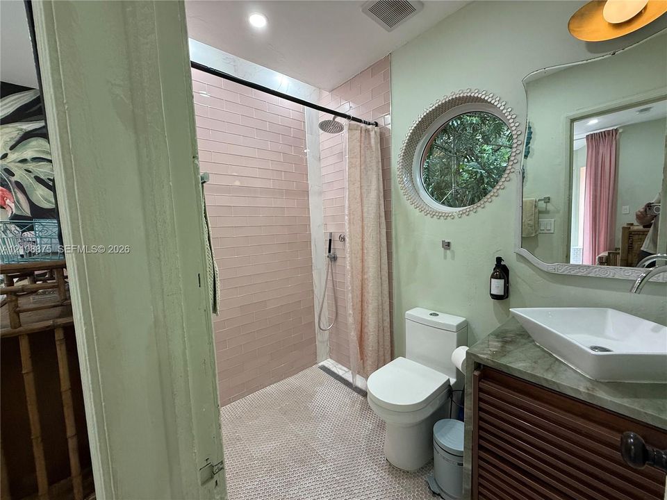 Bathroom featuring a vessel sink with a stone vanity top, a walk-in shower with vertical tile surround, a circular window with decorative trim, and a wall-mounted light fixture