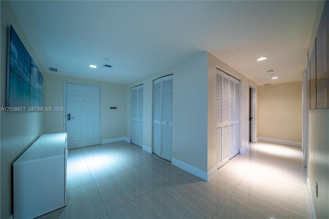 Entry foyer featuring large-format tile flooring, recessed ceiling lighting, and three sets of white louvered-door closets