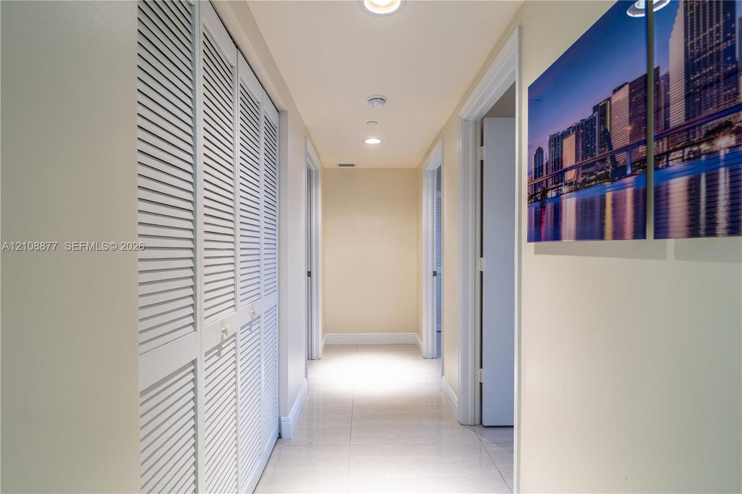 Hallway featuring white louvered-style closet doors, neutral-toned tile flooring, and recessed ceiling lighting