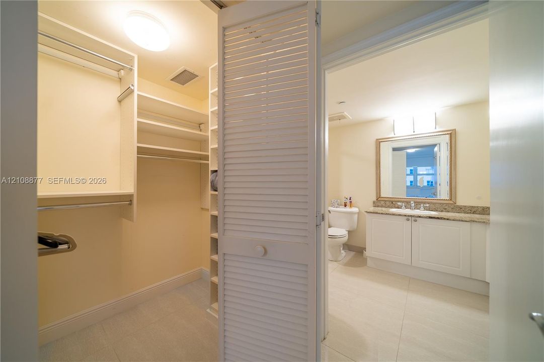 Walk-in closet featuring white built-in shelving and rods, louvered closet door, vanity with stone-finish countertop, integrated sink, and framed mirror