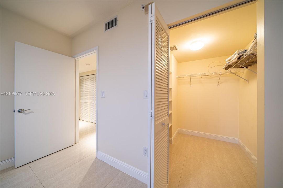 Walk-in closet featuring louvered bi-fold doors, white shelving units, and wire racking, complemented by large-format tile flooring and neutral wall tones