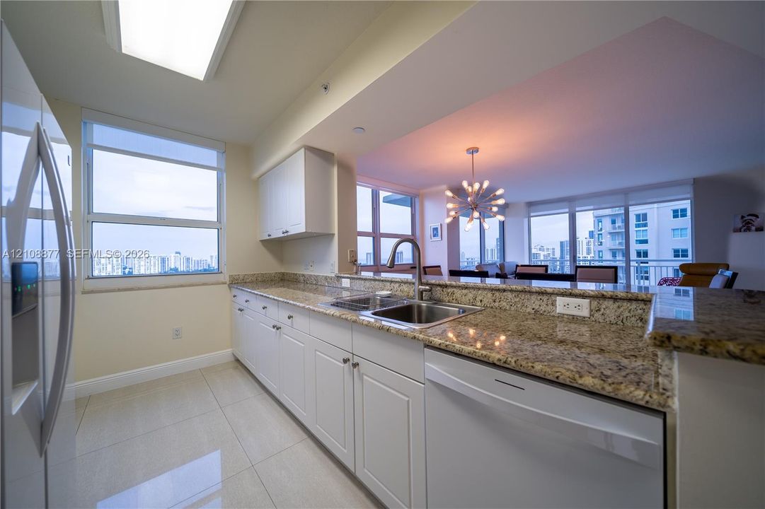 Kitchen featuring white cabinetry, stone-finish countertops, stainless steel dual-basin sink with high-arc faucet, integrated dishwasher, and tile flooring