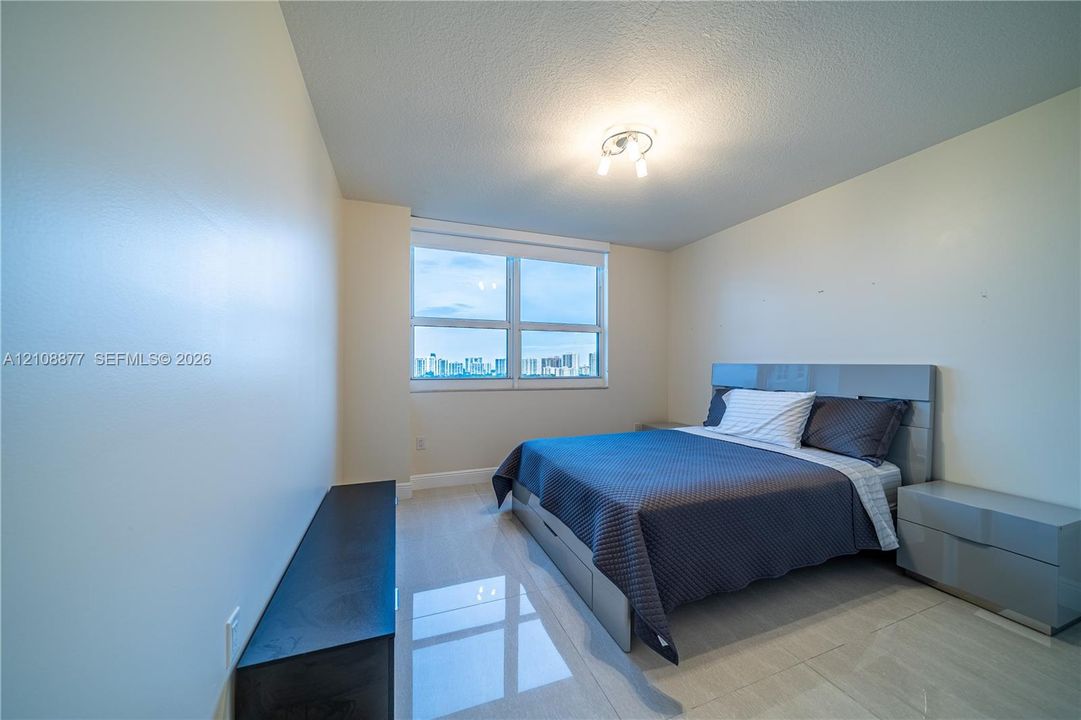 Room featuring large-format tile flooring, neutral wall tones, overhead lighting fixture, and oversized window with urban landscape backdrop